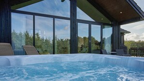 A hot tub with clear blue water, surrounded by large windows offering a view of trees and a building. - 8 Person Holiday Home in Aakirkeby (Akirkeby)