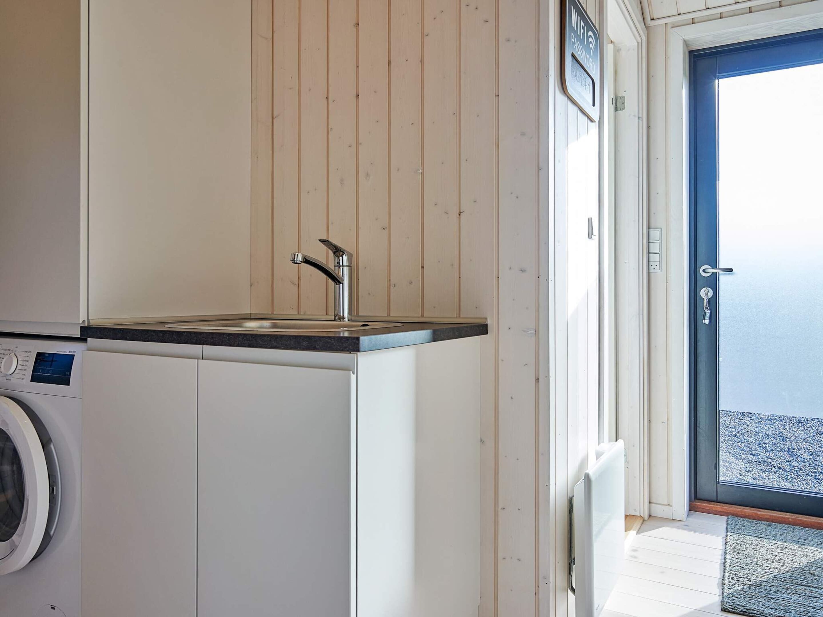 A compact kitchen with a sink, a washing machine, and a door leading to a balcony.