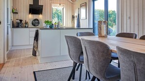 Et moderne køkken med træpaneler, en central ø, hængende lamper og et spiseområde med grå polstrede stole.