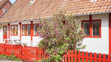 A traditional white building with red accents, a red picket fence, and a flowering tree.