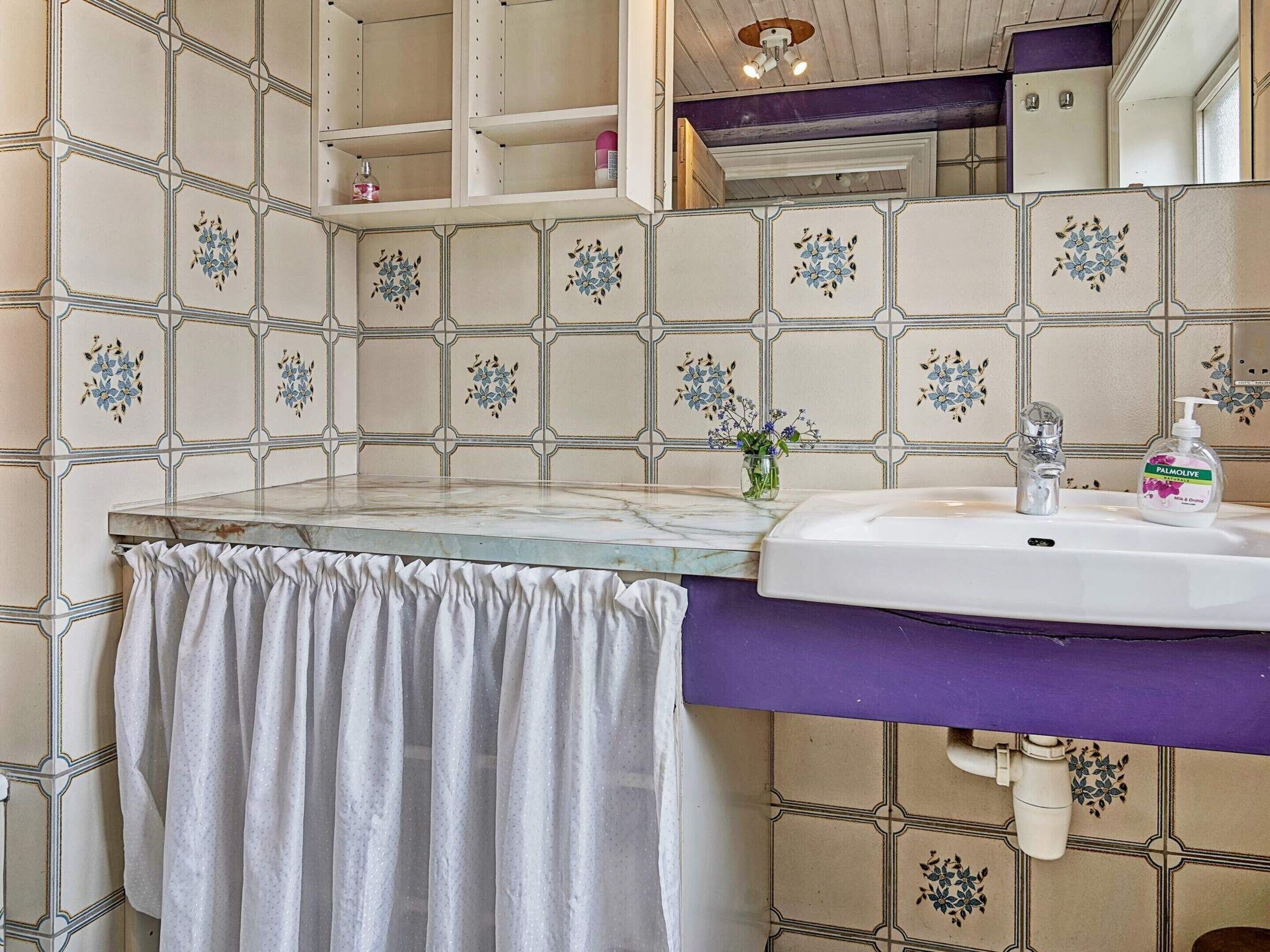 Un baño con encimera de mármol, un lavabo blanco y una pileta morada. Hay una toalla colgada en la pared y un espejo sobre el lavabo.
