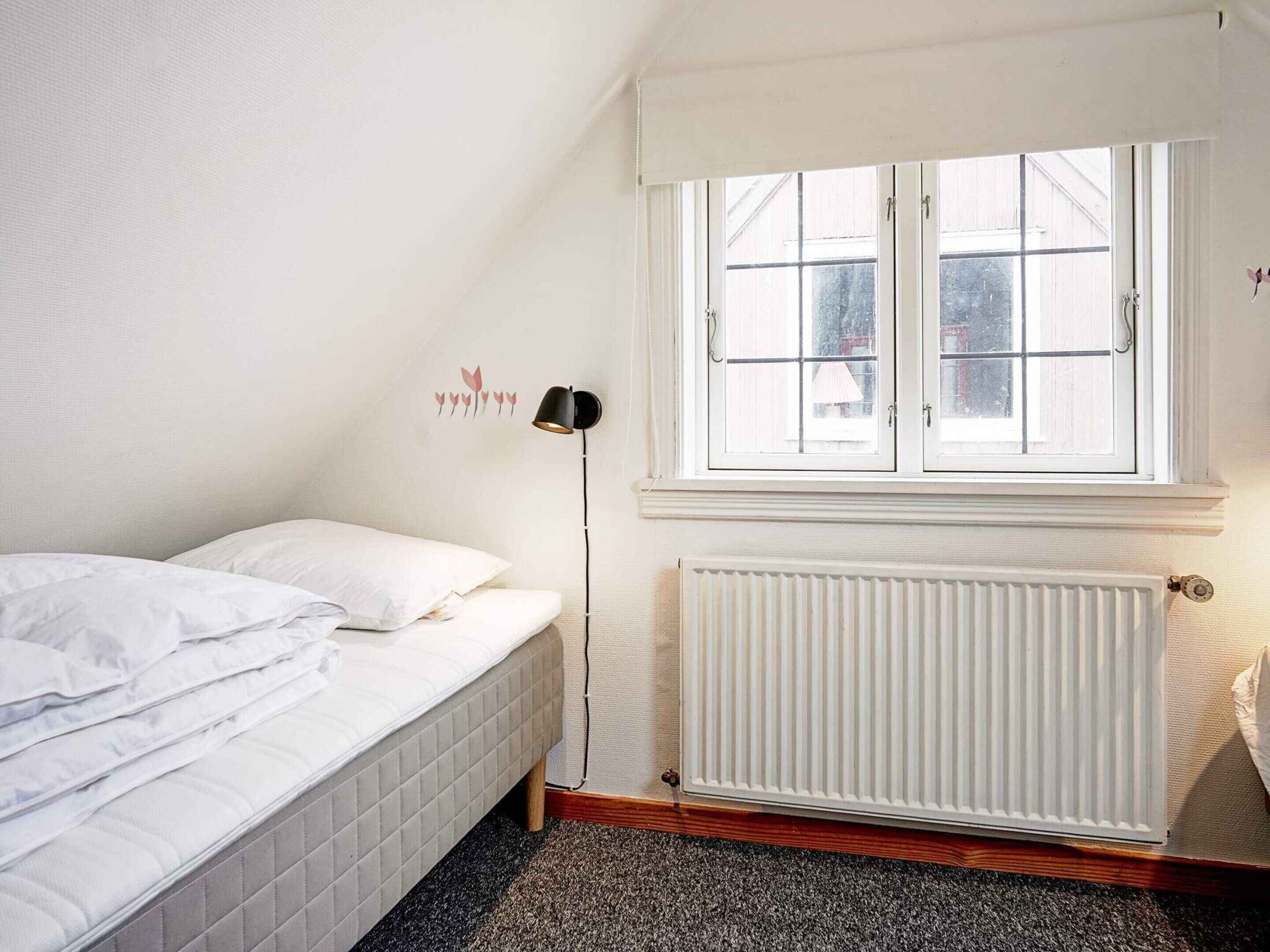 A bedroom with a bed, a radiator, and a window with a view of the outside.