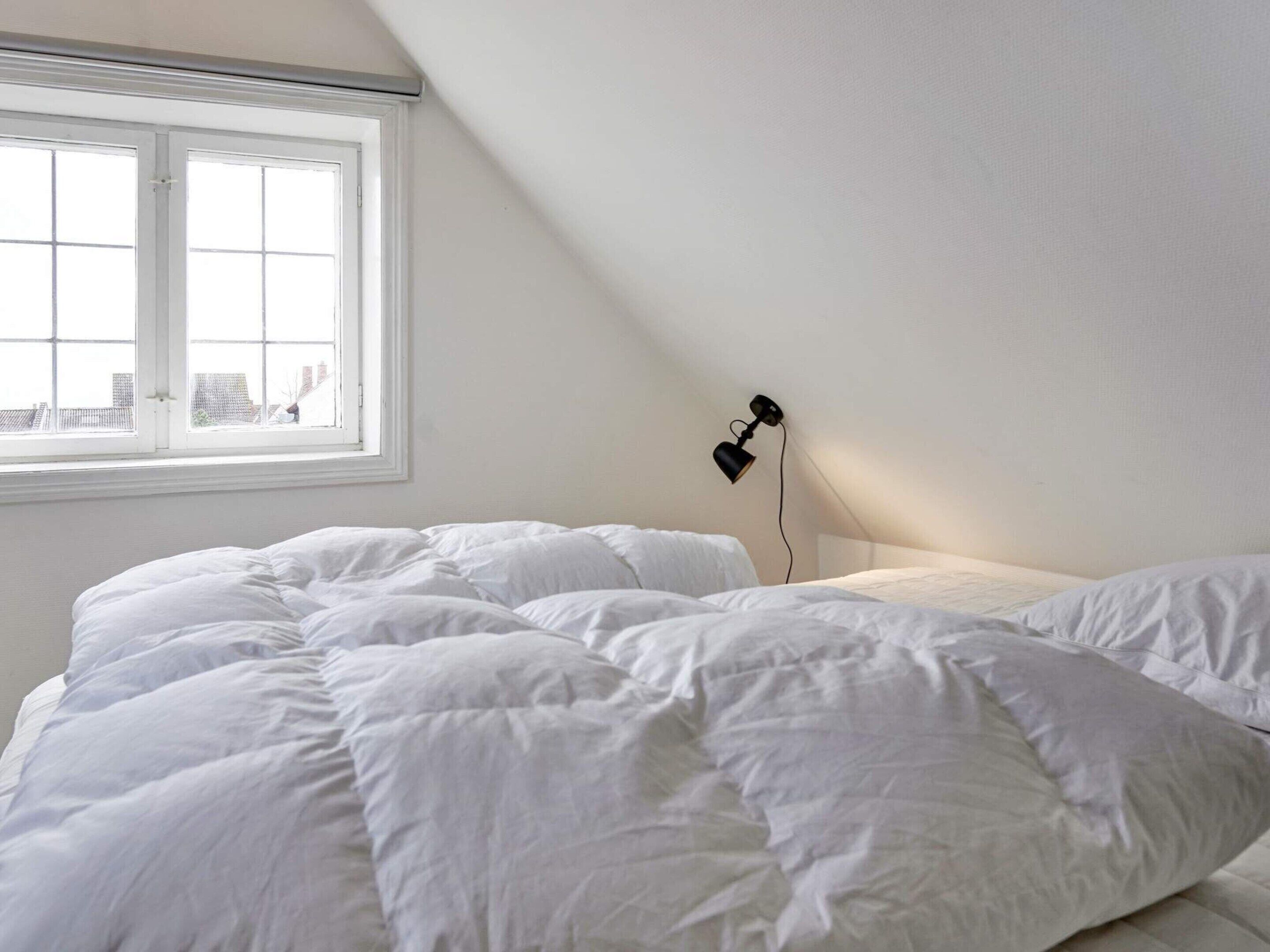 A bedroom with a large bed, a window, and a wall-mounted lamp.