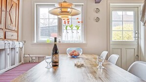 Un coin repas avec une table en bois, une bouteille de vin, des verres et un saladier de fruits.