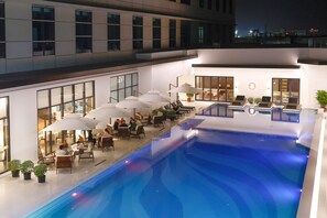 Relax by the rooftop pool surrounded by lounge chairs and umbrellas, or enjoy meals at adjacent tables.