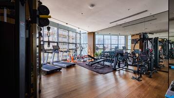 A modern gym with various exercise equipment, large windows, and a wooden floor.