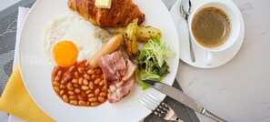 Savor a hearty breakfast with a plate of eggs, croissants, bacon, roasted potatoes, and a fresh salad, paired with a warm cup of coffee.