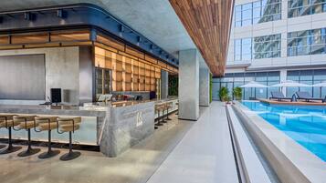 A modern bar area with a poolside view, featuring a bar counter, seating, and a pool.