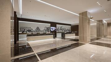 A modern reception area with marble flooring, a reception desk, and wall-mounted artwork depicting architectural structures.