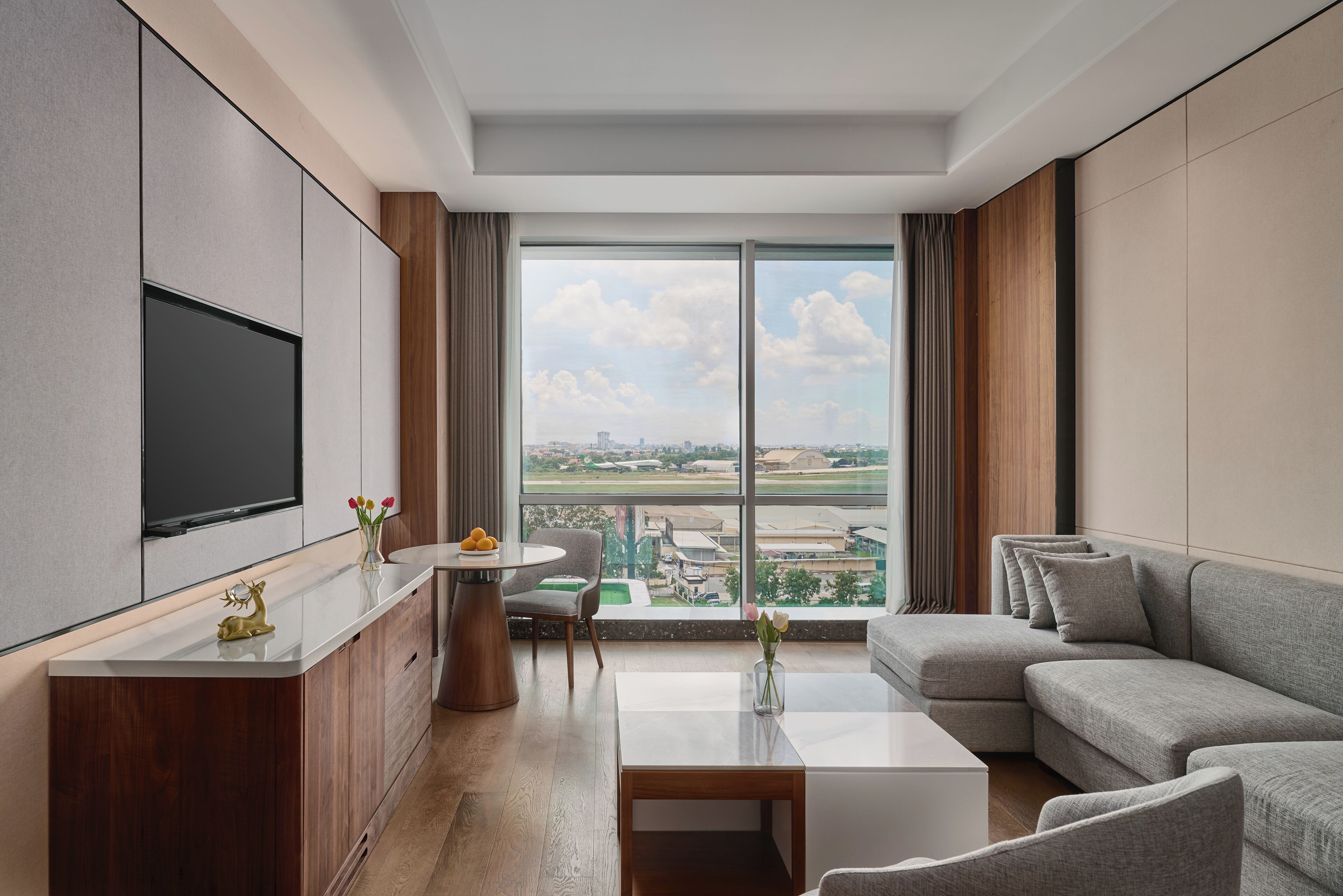 Uma sala de estar moderna com uma televisão de tela plana, um sofá, uma mesa de centro e vista para o horizonte urbano por grandes janelas.
