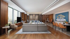Un salon moderne avec un grand canapé d’angle, un téléviseur et un coin repas doté de chaises orange.
