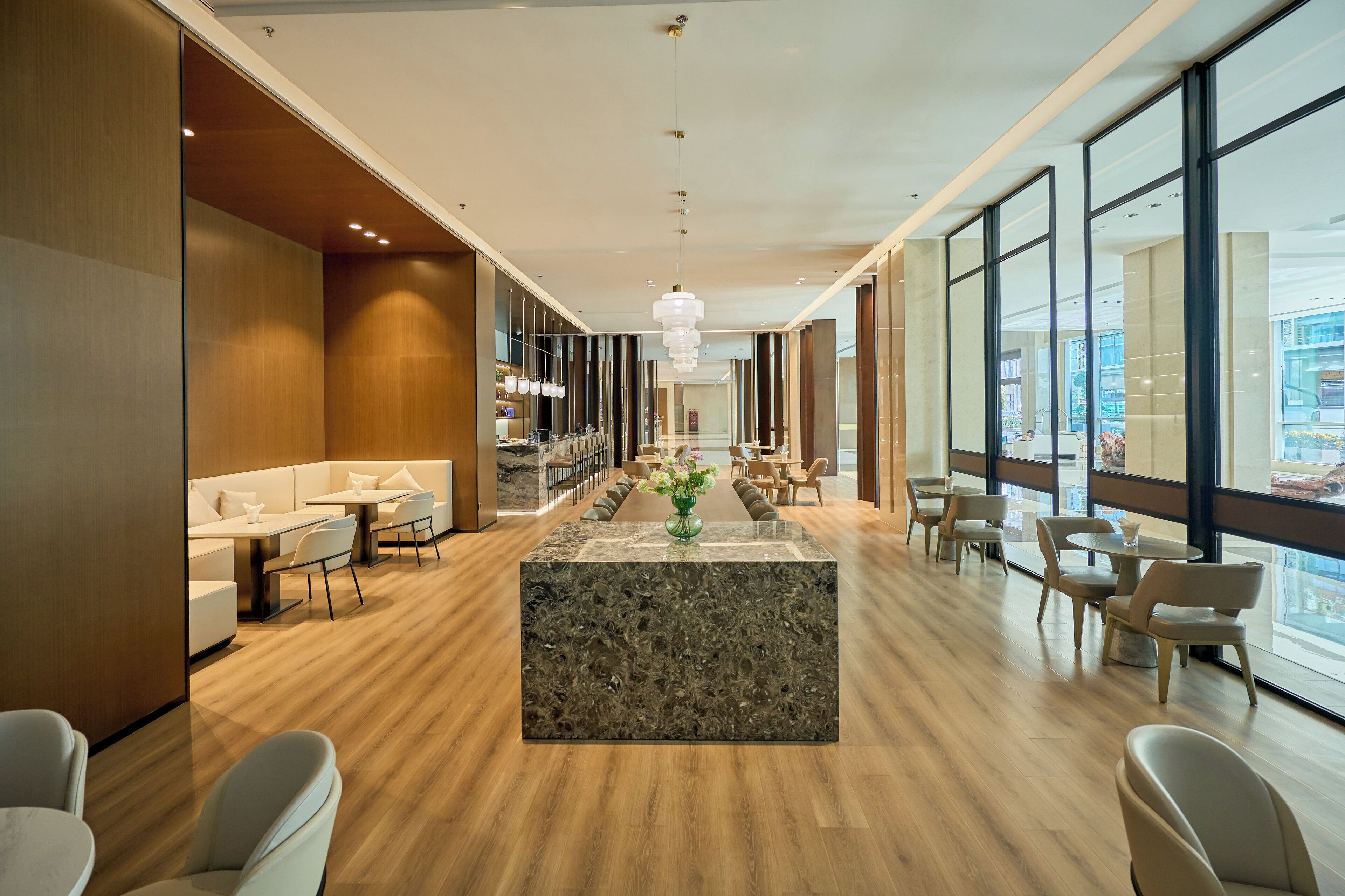 A modern hotel lobby with a central marble reception desk, seating areas, and large windows offering views of the city.