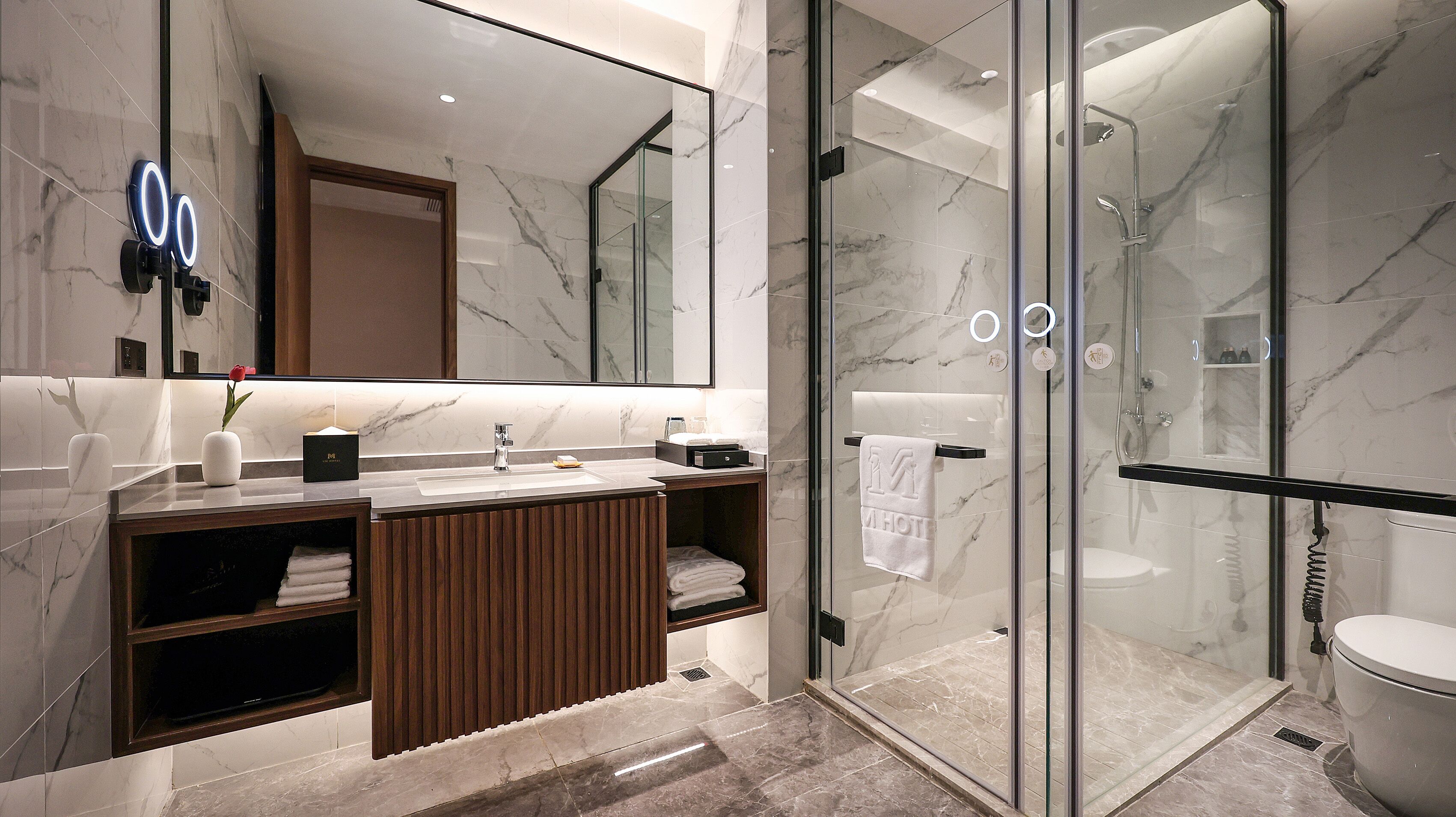 A modern bathroom with a glass-enclosed shower, a marble-tiled vanity, and a large mirror.