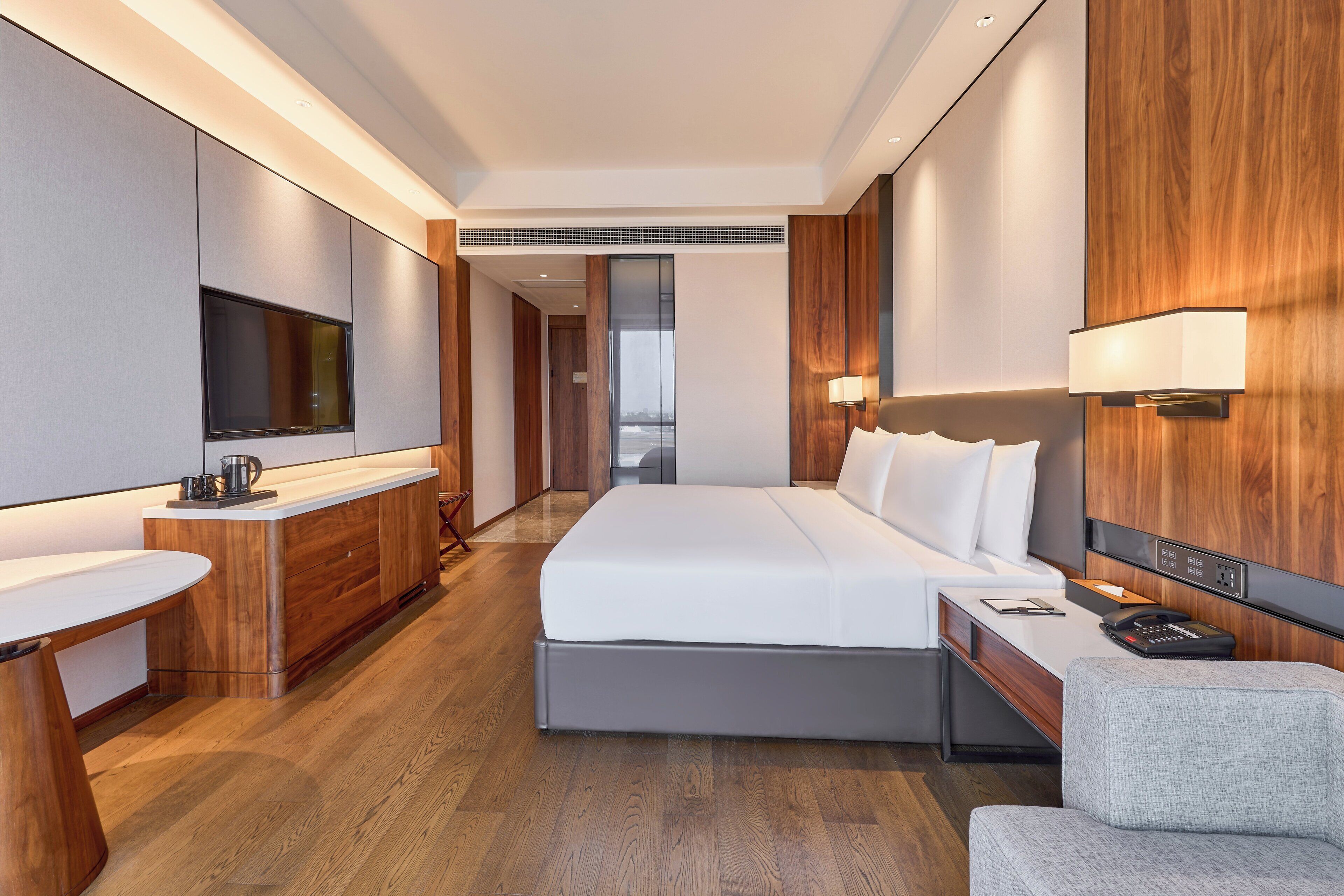 Une chambre d’hôtel moderne avec un grand lit, une table de chevet avec une lampe, un téléviseur fixé au mur et une armoire en bois.