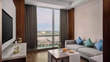 A modern living room with a large window, a grey sofa, a coffee table, and a flat-screen TV.