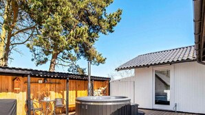 A wooden deck with a hot tub, a covered seating area, and a building with a tiled roof. - 7 Person Holiday Home in Dannemare (Dannemare)
