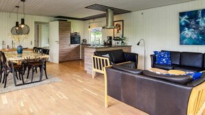 A modern kitchen with a central island, a dining area with a wooden table and chairs, and a living area with a sofa and a coffee table. - 7 Person Holiday Home in Dannemare (Dannemare)