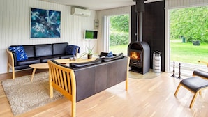 A modern living room with a black leather sofa, a wooden coffee table, and a black fireplace. - 7 Person Holiday Home in Dannemare (Dannemare)