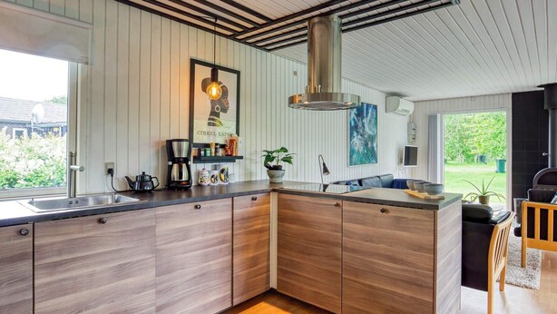 A modern kitchen with a large island, wooden cabinets, and a hanging light fixture. - 7 Person Holiday Home in Dannemare (Dannemare)