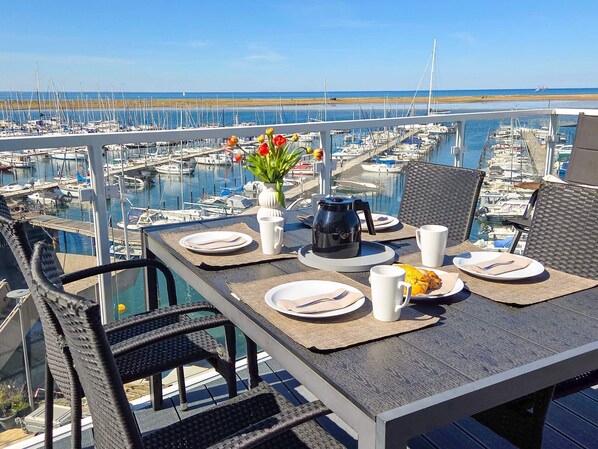 A dining table with plates, cutlery, and a coffee pot, overlooking a marina with boats.