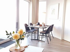 Un comedor moderno con una mesa dispuesta para cuatro personas, sillas alrededor y un florero sobre la mesa.