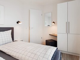 Un dormitorio con cama, armario, espejo y mesita de noche.