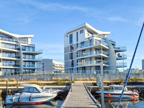 A modern building with multiple balconies, a dock with boats, and a clear sky. - 5 Star Holiday Home in Wendtorf (Wendtorf)