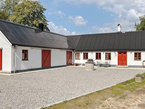 A building with a gravel courtyard, red doors, and a black roof. - 4 Person Holiday Home in Skurup (Skurup)