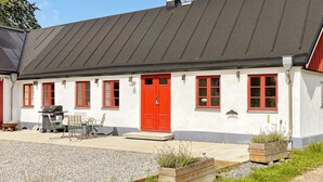 A white building with red doors and windows, a chimney, and outdoor seating.