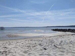 A beach with a sandy shore, calm water, and a pier in the distance. - 4 Star Holiday Home in Ebeltoft (Ebeltoft)