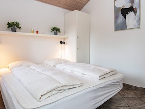 A bed with white bedding, a bedside lamp, and a shelf with plants and toiletries.