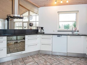 Una cocina moderna con armarios blancos, campana extractora de acero inoxidable y un amplio ventanal que proporciona luz natural.