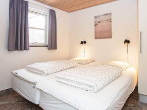 Un dormitorio con dos camas, una ventana con cortinas, una lámpara de pared y una pintura de paisaje desértico.