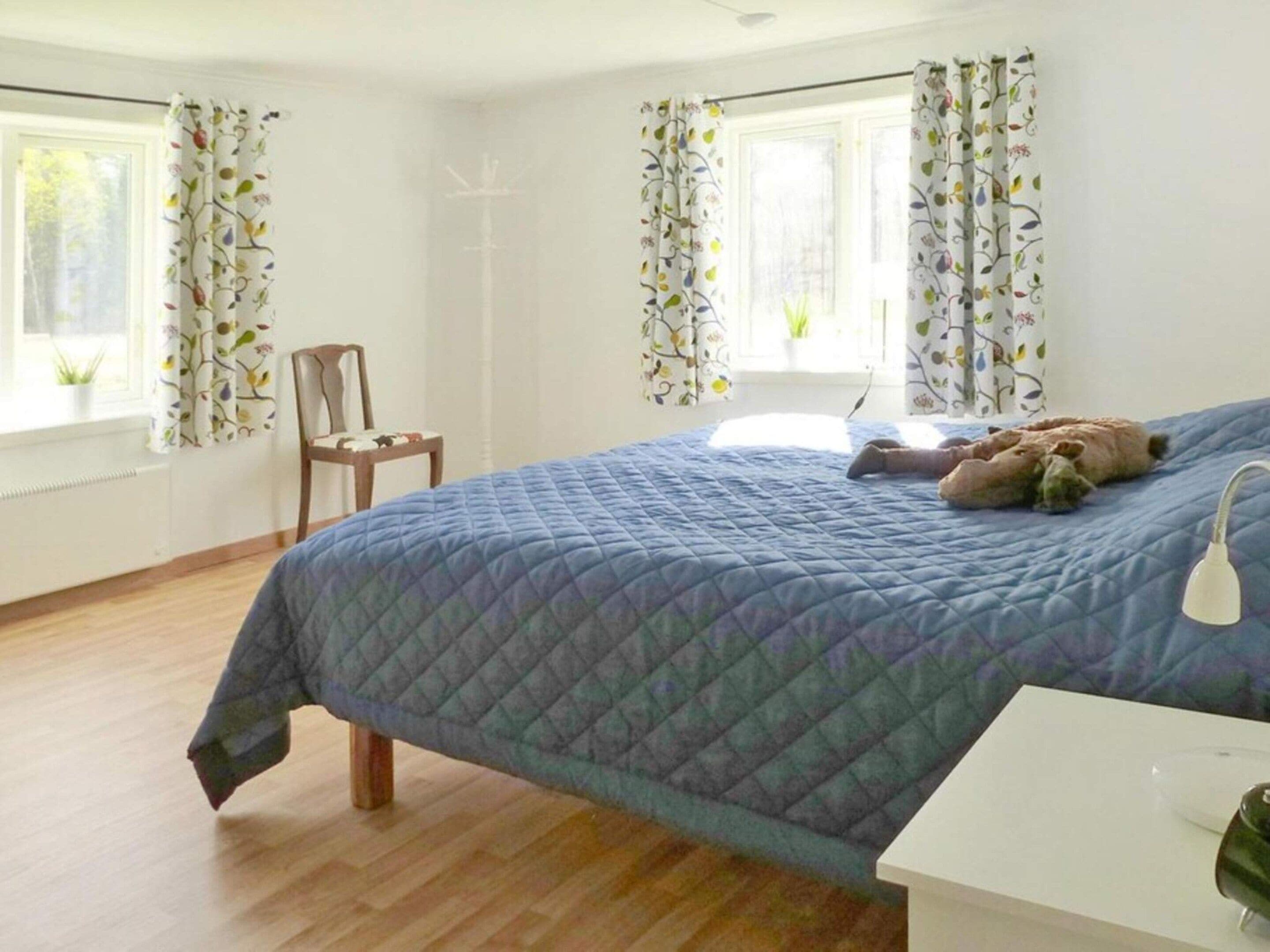 A bedroom with a bed, a chair, a bedside table, and curtains.