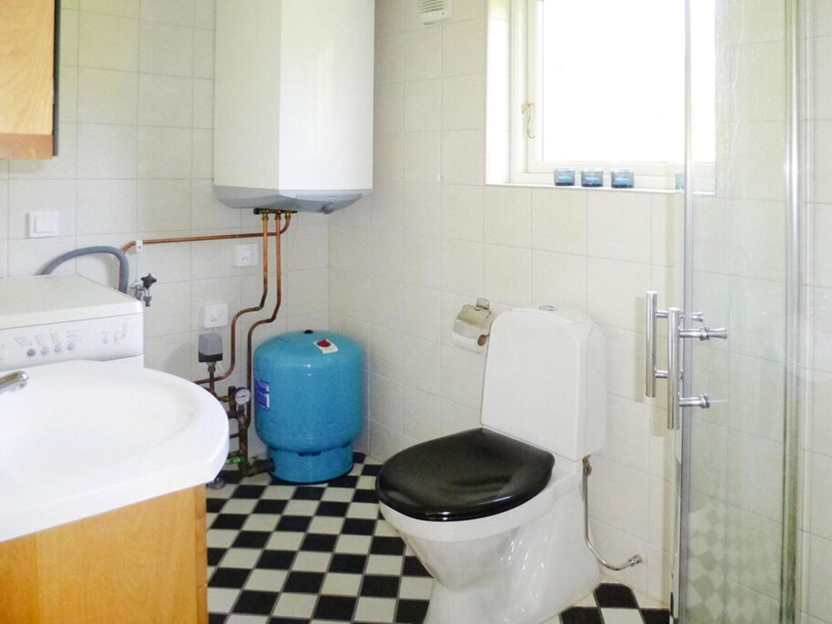 A bathroom with a white toilet, a blue water heater, a sink, and a shower area.