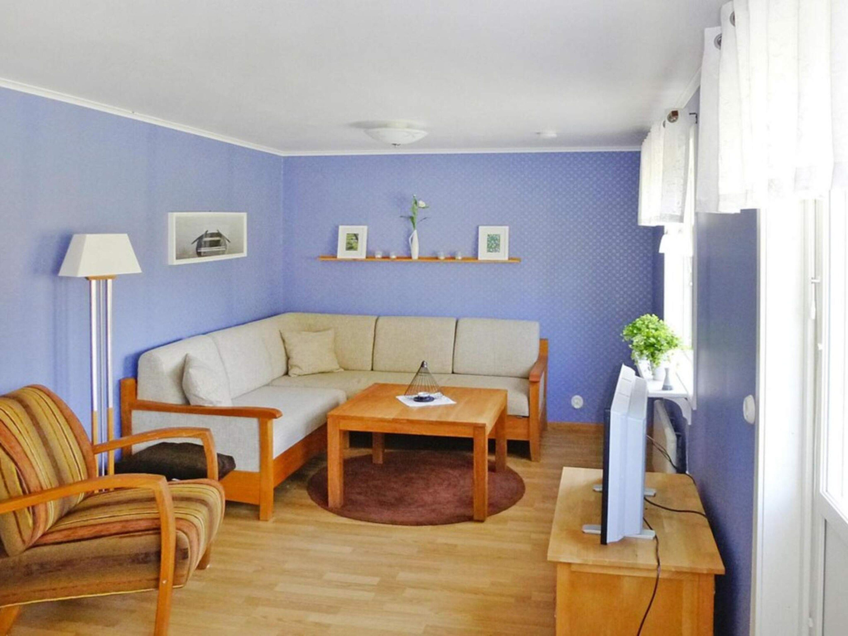 Ett vardagsrum med en soffa, en fåtölj, ett litet bord, en lampa och en tv som står på ett TV-bord.