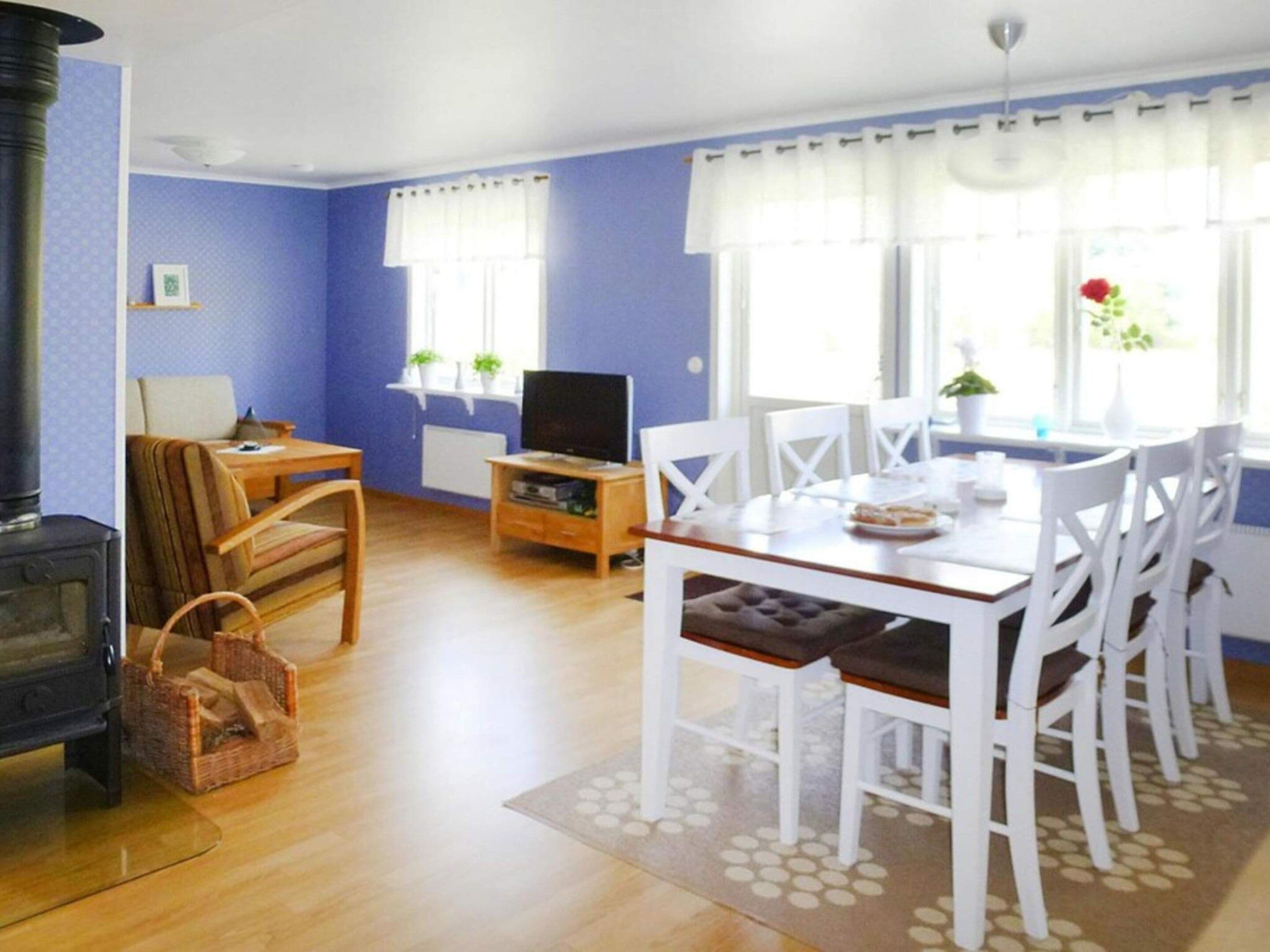 A room with a dining table, chairs, a television, a fireplace, and a window with curtains.