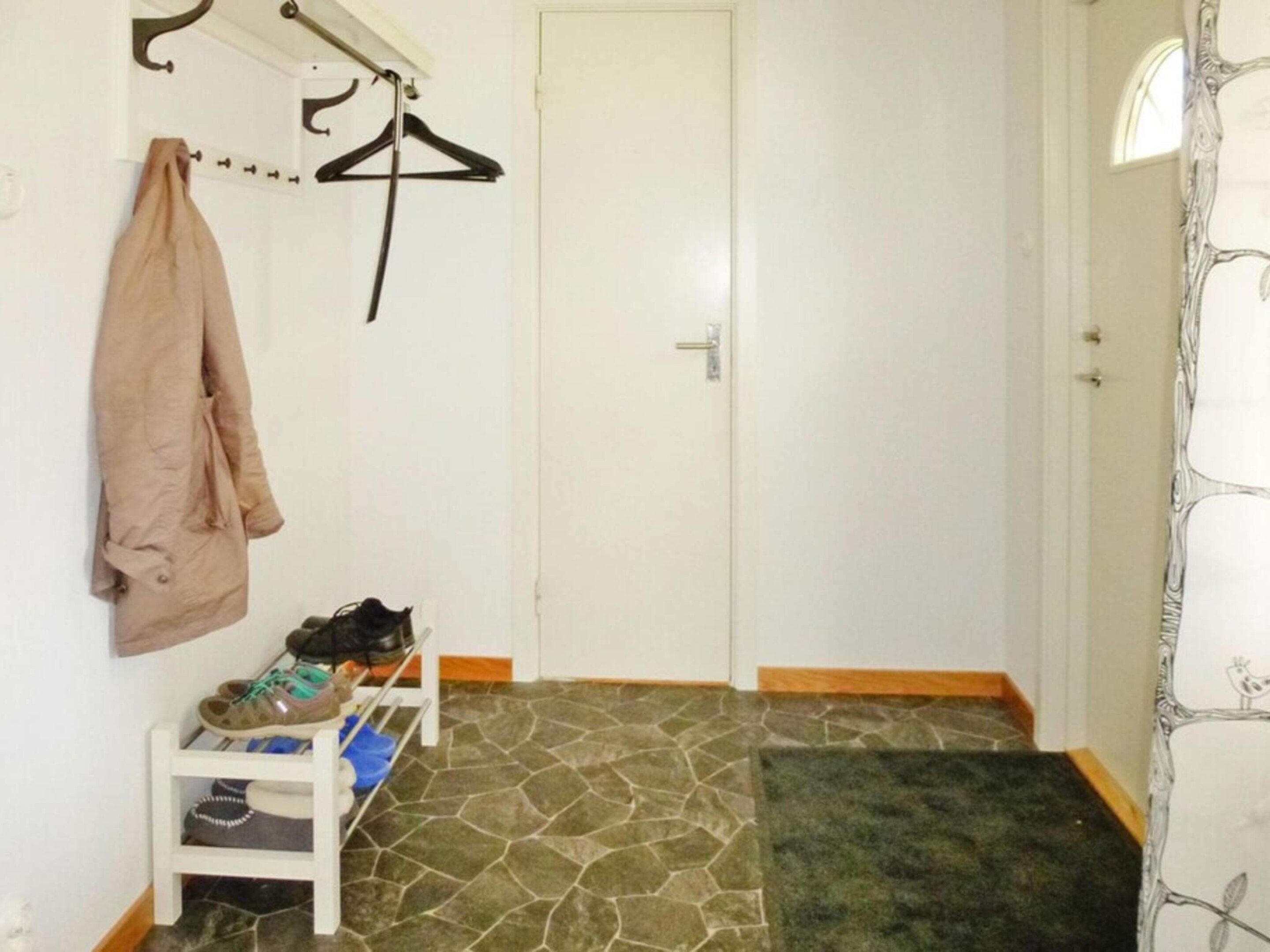 A hallway with a coat rack, a door, a shoe rack, and a patterned floor.