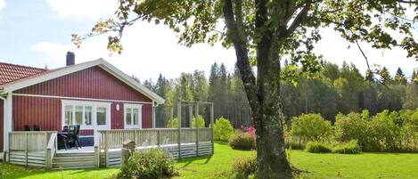 A red house with a fenced yard and a large tree in front.