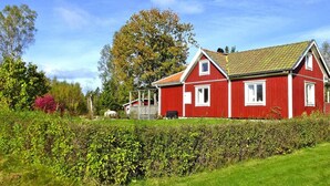 Ett rött hus med ett sluttande tak, omgivet av grönska och en häck.
