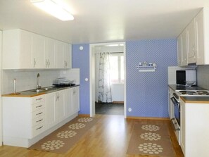 A kitchen with white cabinets, a microwave, and a stove. There is a window with curtains and a door leading to another room. - 4 Person Holiday Home in Bralanda (Bralanda)