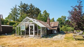 A rustic glass greenhouse with a brick chimney, surrounded by a dry grassy area and trees. - 6 Person Holiday Home in Ebeltoft (Ebeltoft)