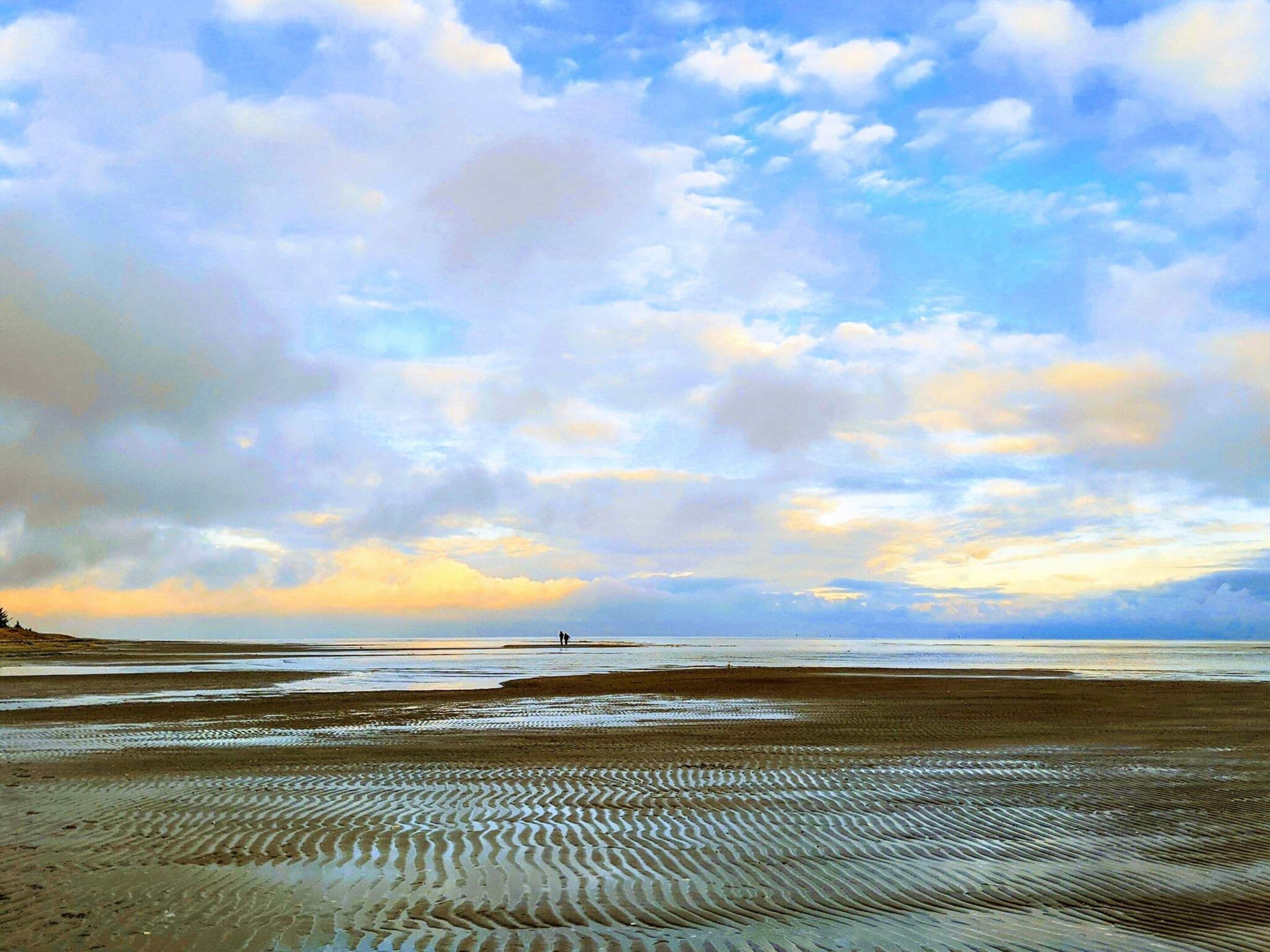 A beach with a wide sandy area and a person standing in the distance.