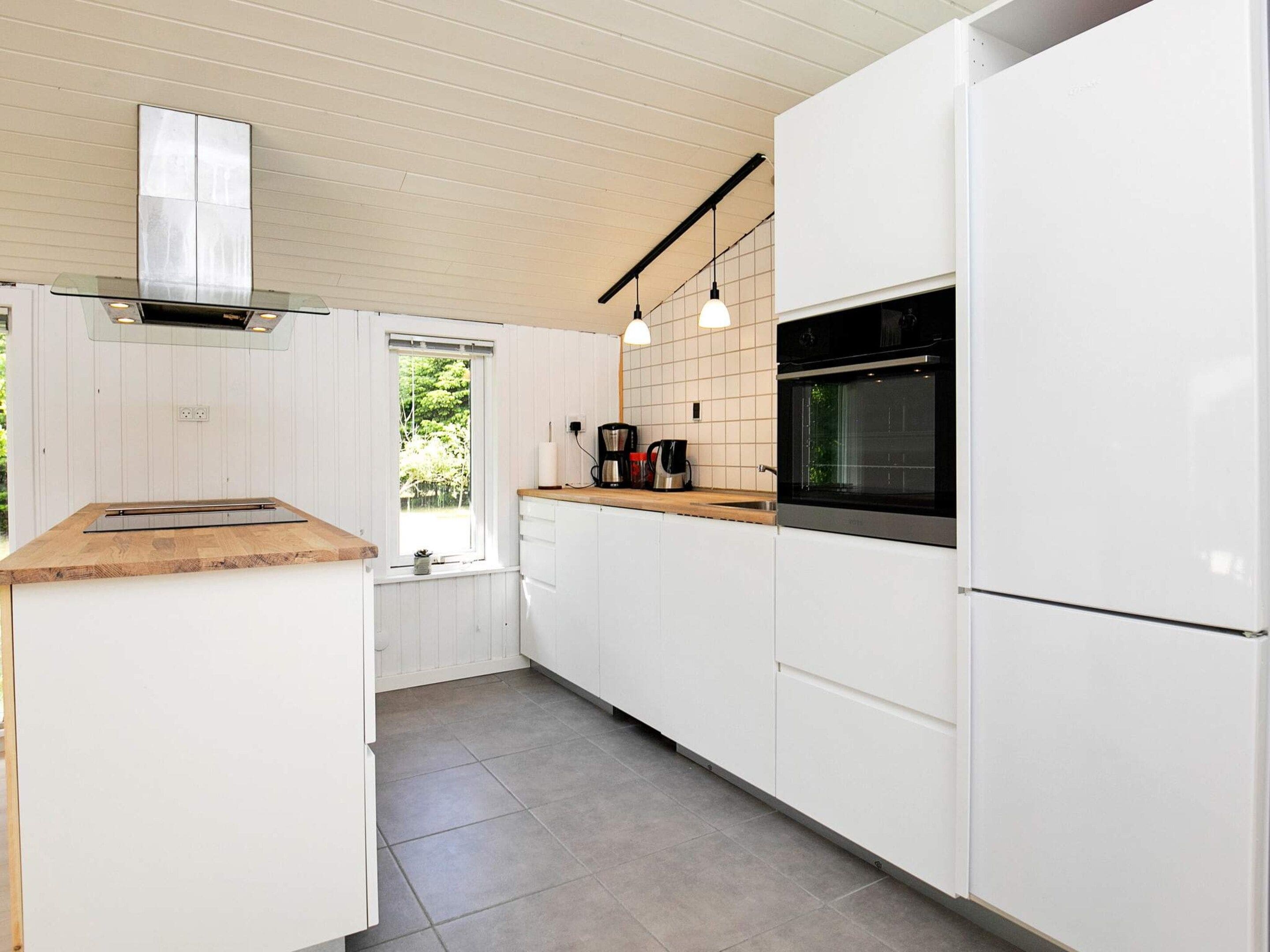 A modern kitchen with white cabinetry, a wooden countertop, a built-in oven, and pendant lighting.
