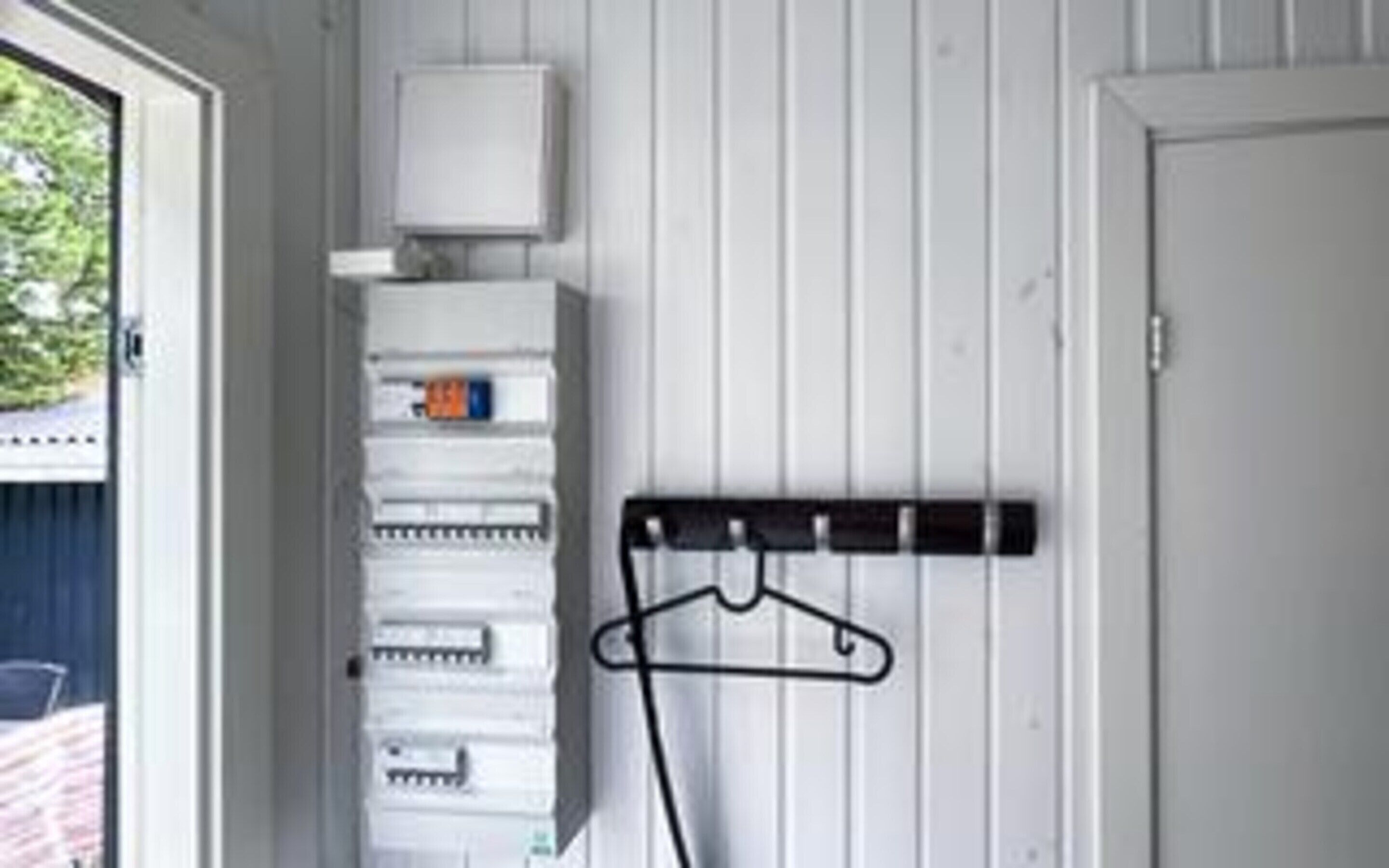 Une pièce avec un mur blanc, une porte, une fenêtre et un porte-manteau.