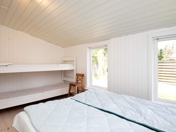 Une chambre avec des lits superposés, un lit simple, une chaise et une fenêtre donnant sur les arbres.