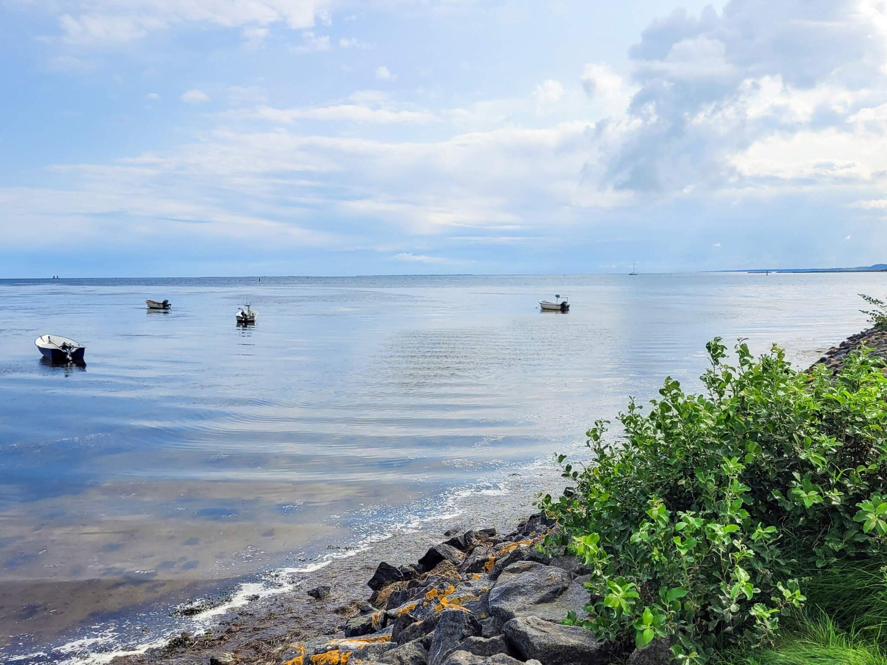 A coastal scene with calm waters, boats, and rocky shoreline.