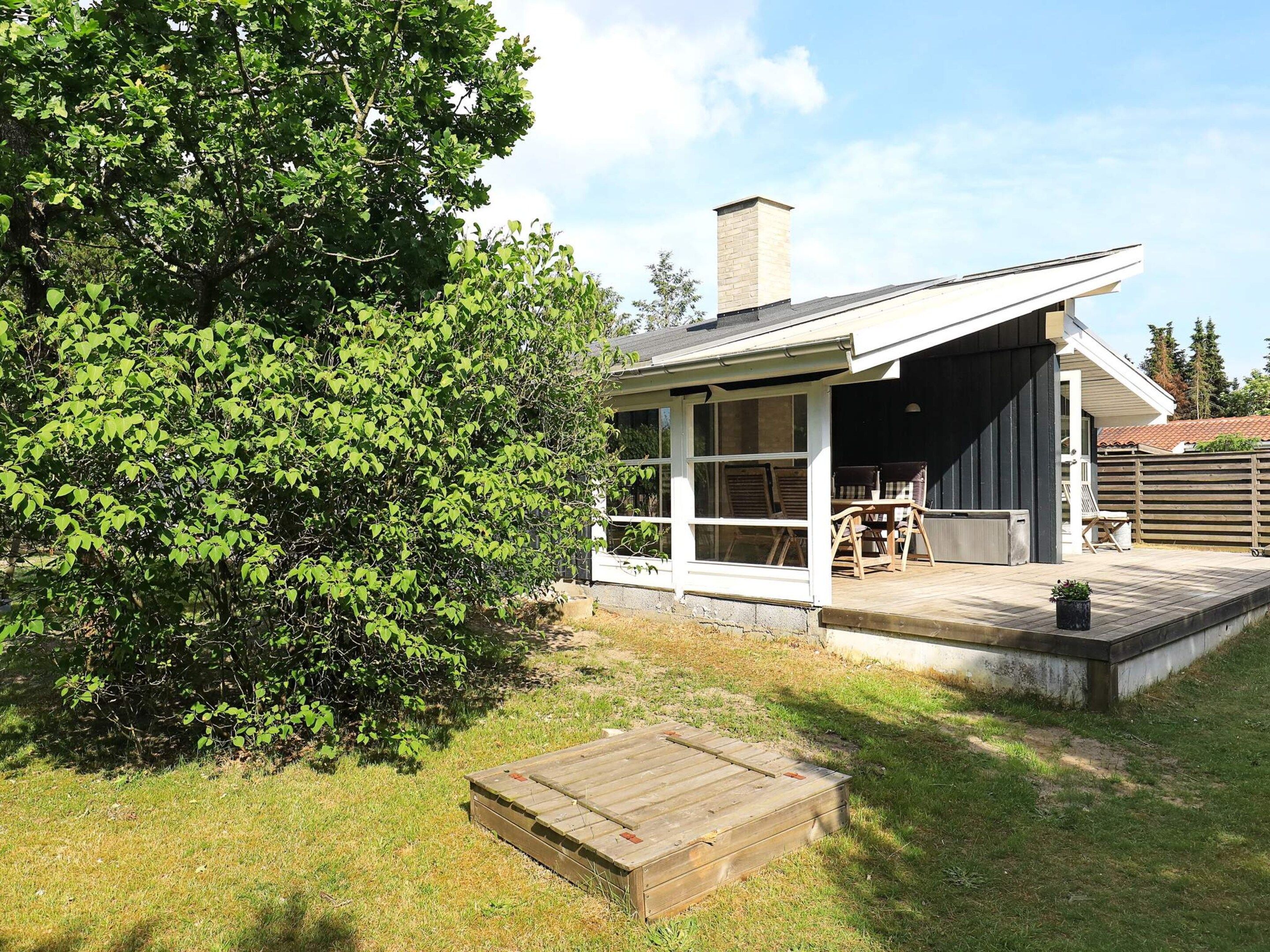 A modern house with a covered patio, a wooden deck, and a large tree in the backyard.