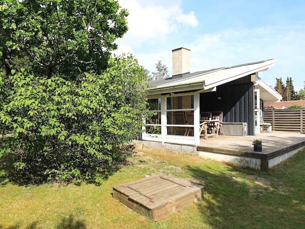 A modern house with a covered patio, a wooden deck, and a large tree in the backyard.