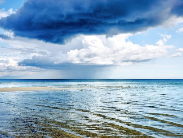 A beach with clear water, a sandy shore, and a cloudy sky.